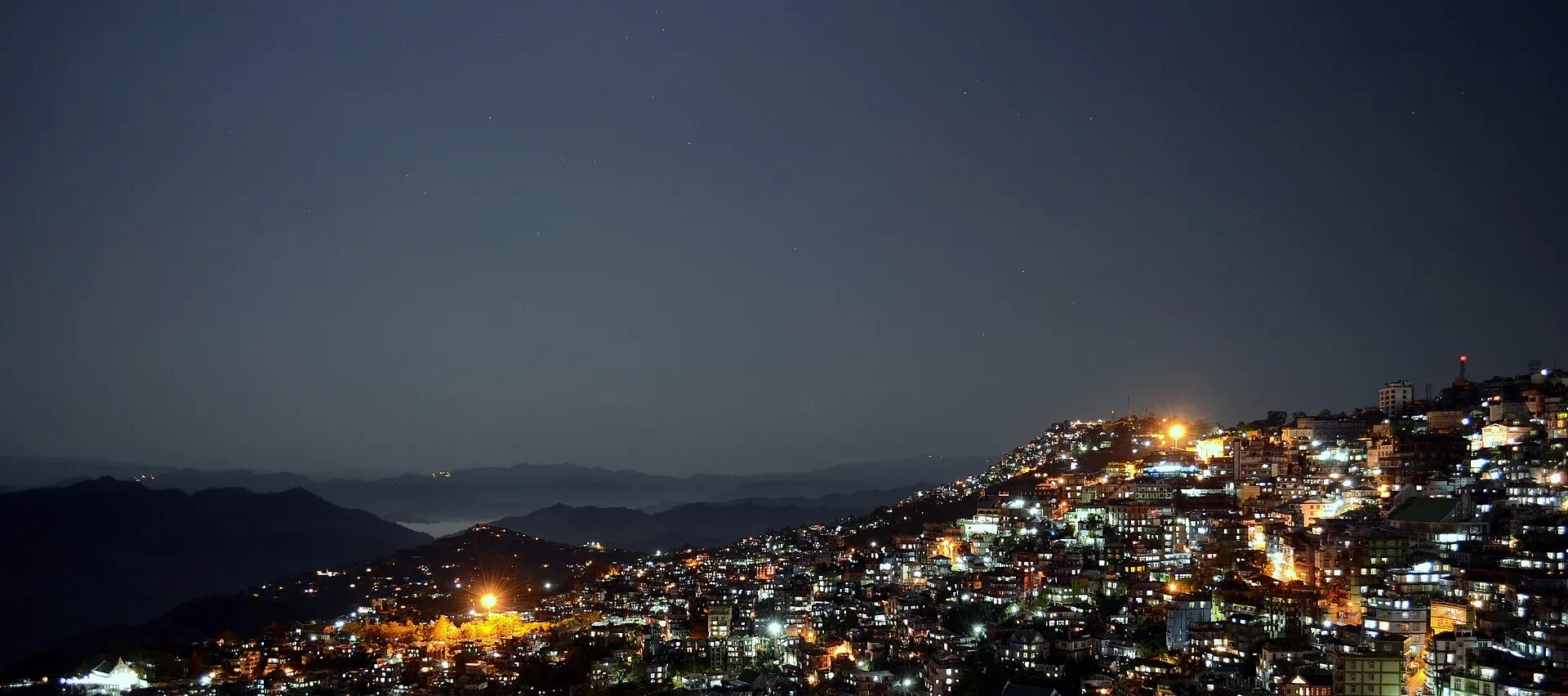 Aizawl at night, thousands of lights tracing the city down its ridgeline with moonlit ranges fading into the distance
