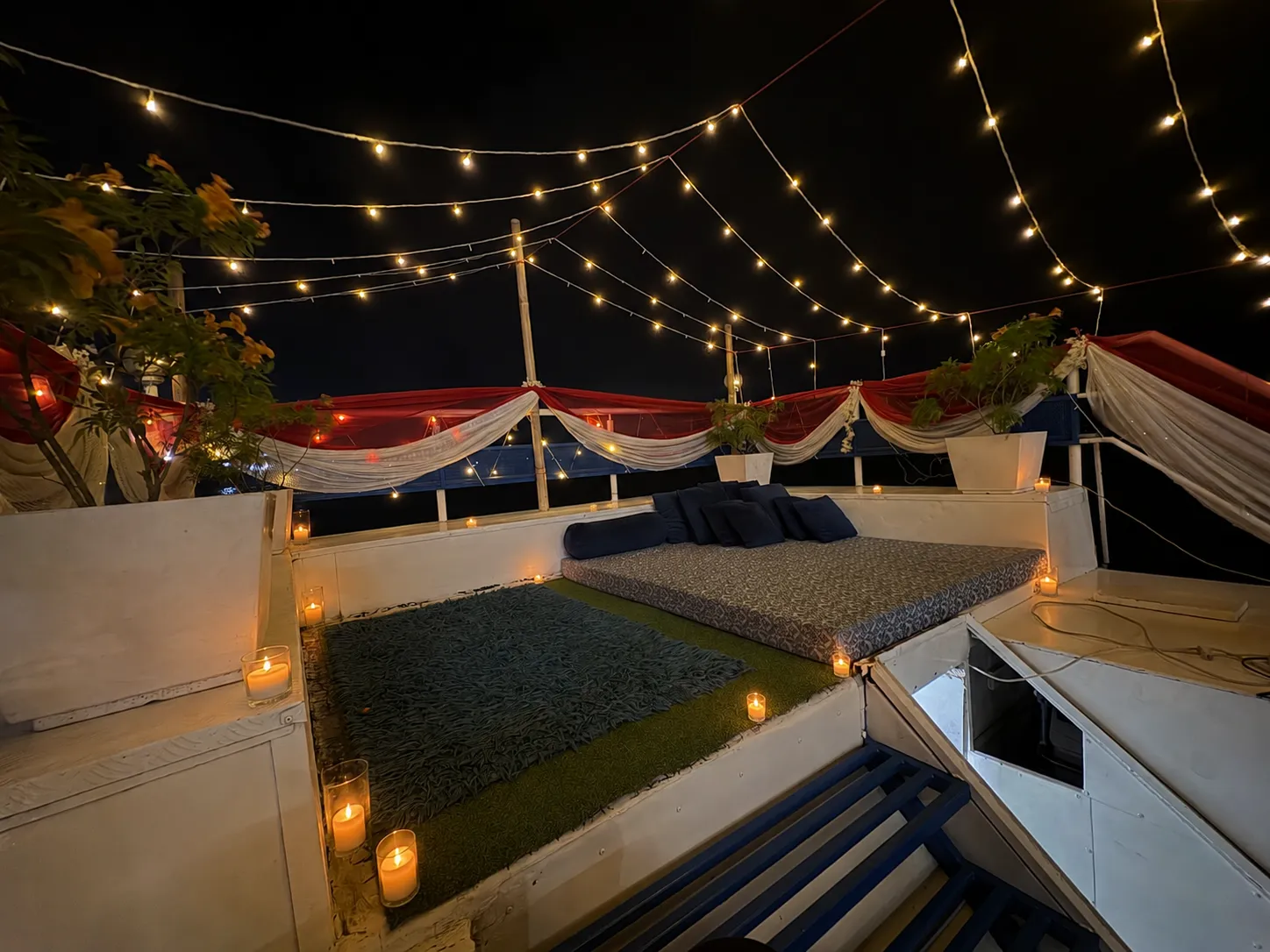 Cushioned lounge dressed with fairy lights and candles on the S B Agam deck at night