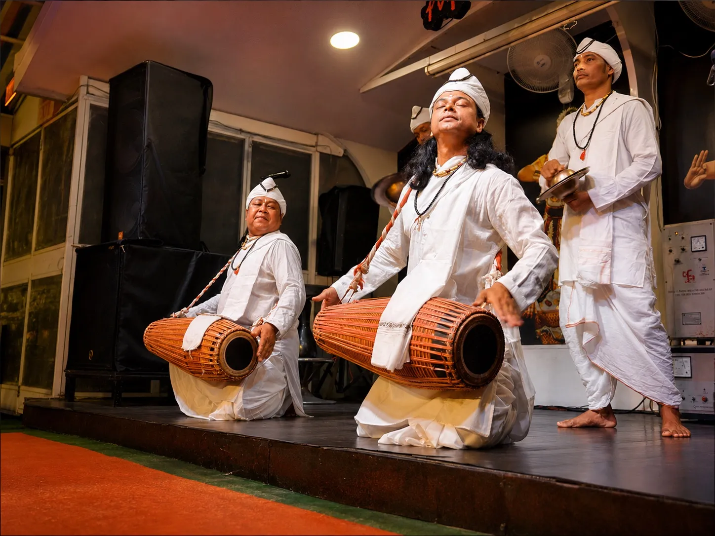 Gayan Bayan performers in white robes and turbans playing khol drums and cymbals on the dinner cruise stage